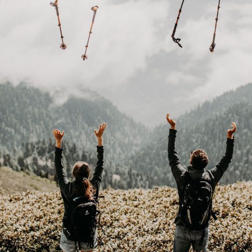 Zwei Wanderer mit Aussicht auf die Berge werfen Wanderstöcke in die Luft