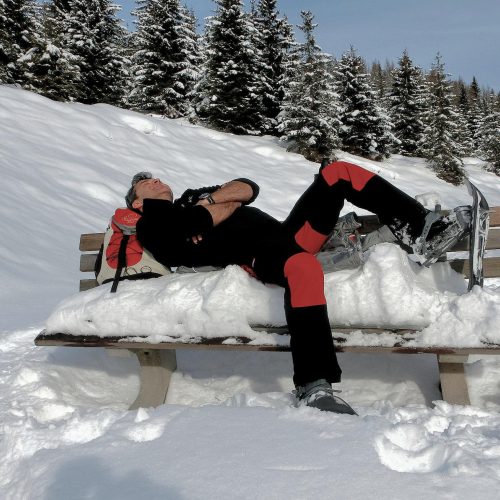 Schneeschuhwanderer ruht sich auf verschneiter Bank aus