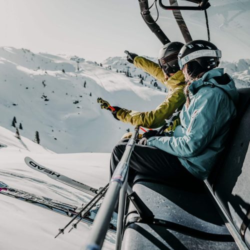Skifahrer in einer Gondel genießen die Aussicht auf die verschneiten Berge